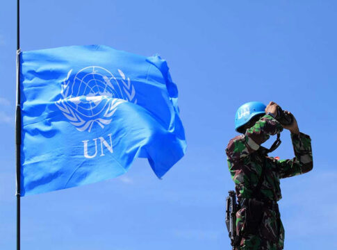 UN soldier with binoculars next to United Nations flag.