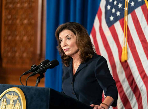 Woman speaking at podium with American flag backdrop.