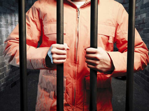 Person in orange jacket behind prison bars.