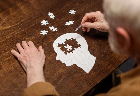Elderly person assembling a head-shaped jigsaw puzzle on a wooden table