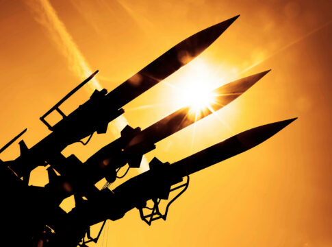 Silhouetted missiles on a launcher against a bright sunset sky