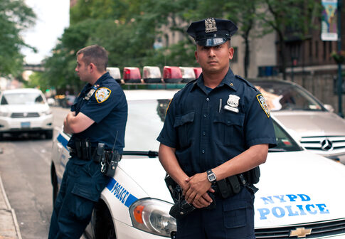 Two NYPD officers standing near a police car in an urban environment