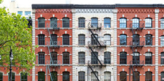 Red-brick building with fire escapes and storefronts, daytime.